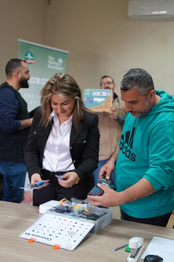Loubnaniyoun team inspecting a robotics classroom kit beside the Stirling Foundation banner