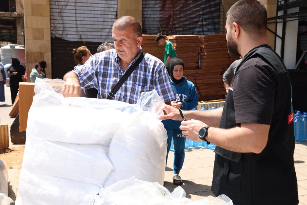 A displaced man receiving bedding and water from a Loubnaniyoun volunteer