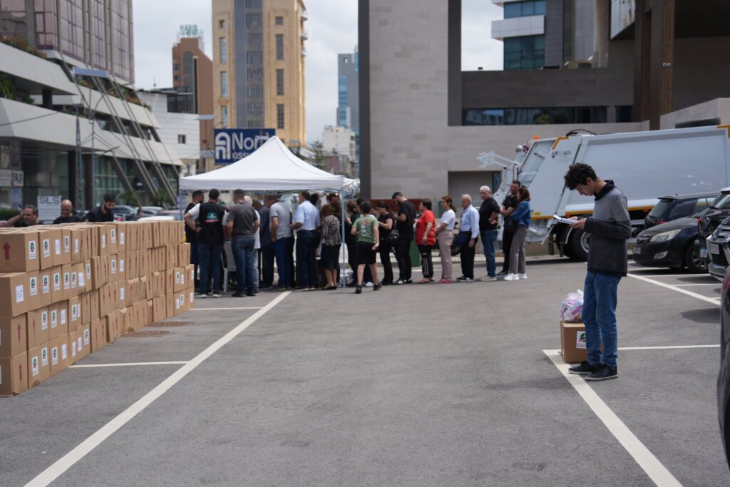 Aid boxes stacked at a Loubnaniyoun distribution point as families line up