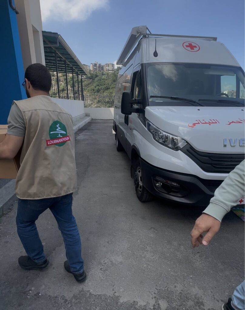 A Loubnaniyoun volunteer loading aid beside a Lebanese Red Cross vehicle